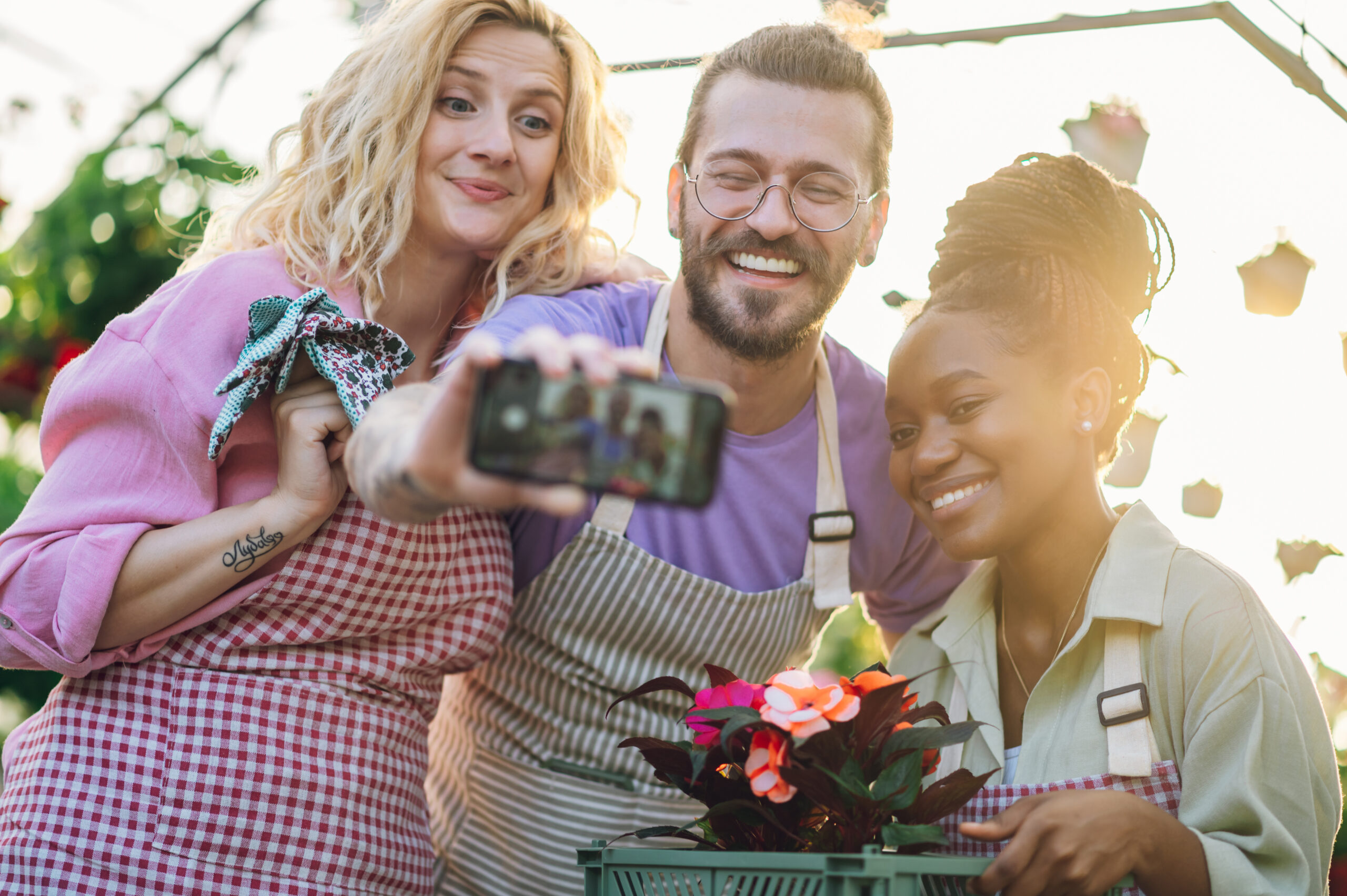 Multiracial group of gardeners working in a greenhouse and taking selfie with a smartphone